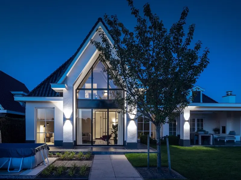 Moderne villa met grote glazen puntgevel, verlicht in de avond